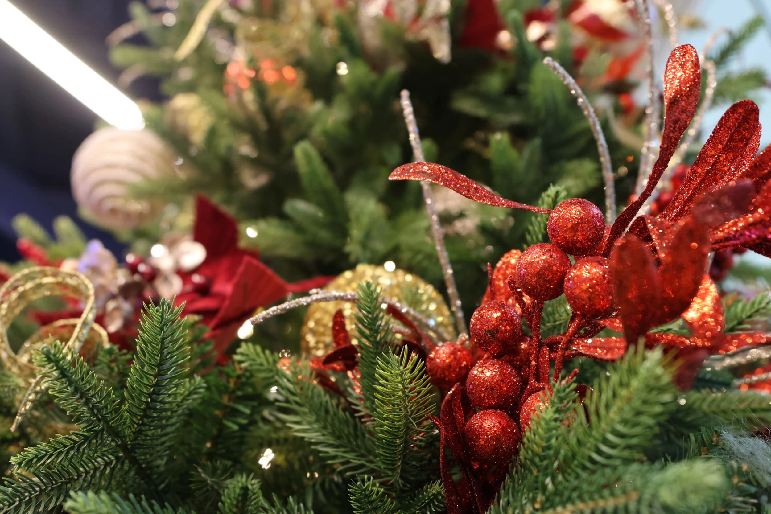 Close-up of a festive Christmas arrangement with green pine branches, red glitter berries, gold ribbons, and ornaments.